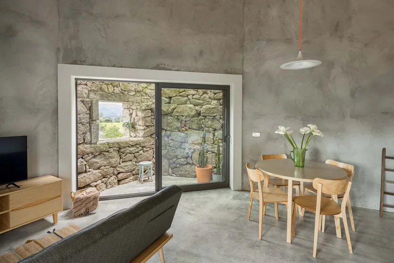 Polished concrete floor and dining table framed by glazed opening revealing the stone wall courtyard beyond