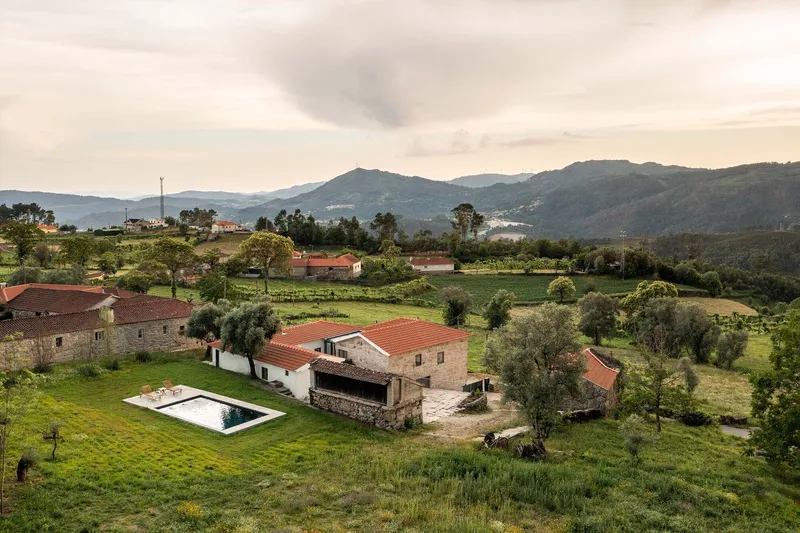 Renovated stone farmhouse complex with red tile roofs and swimming pool in hilly landscape at dusk