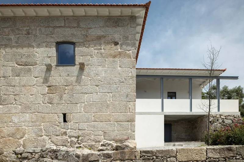 Stone masonry wall of a traditional granary building adjacent to a white rendered extension with a terrace