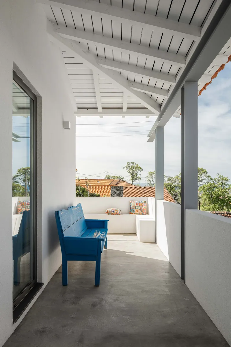 Covered terrace with painted timber ceiling, exposed rafters, and a blue bench overlooking clay-tiled rooftops