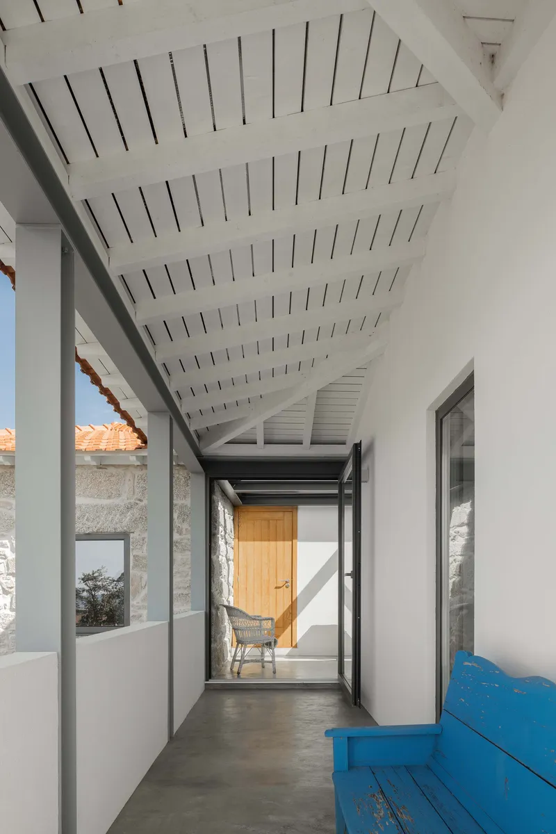 Corridor with slatted white timber ceiling connecting to a timber door framed by a dark steel beam