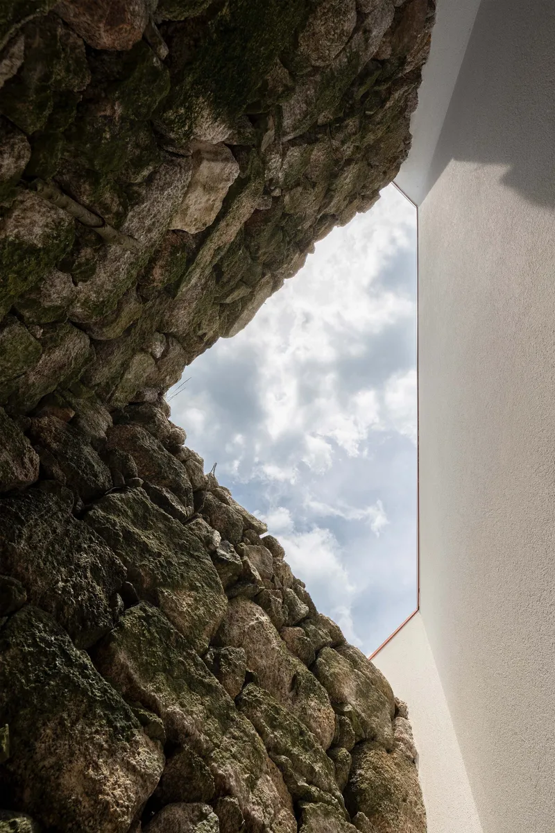 Detail of the white rendered wall edge meeting moss-covered granite stone masonry below scattered clouds