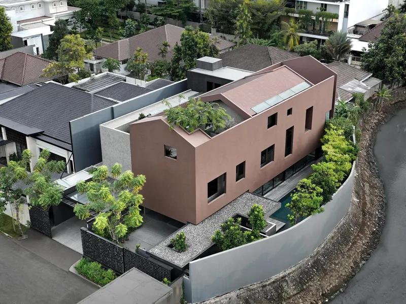 Aerial view of terracotta-rendered volume with rooftop garden surrounded by tiled-roof houses