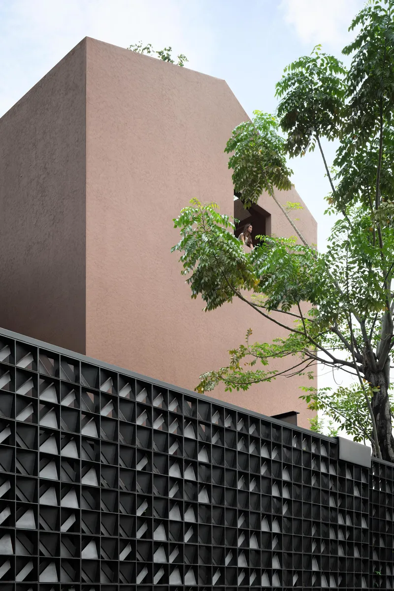 Terracotta facade rising above black geometric perforated screen wall with trees in foreground
