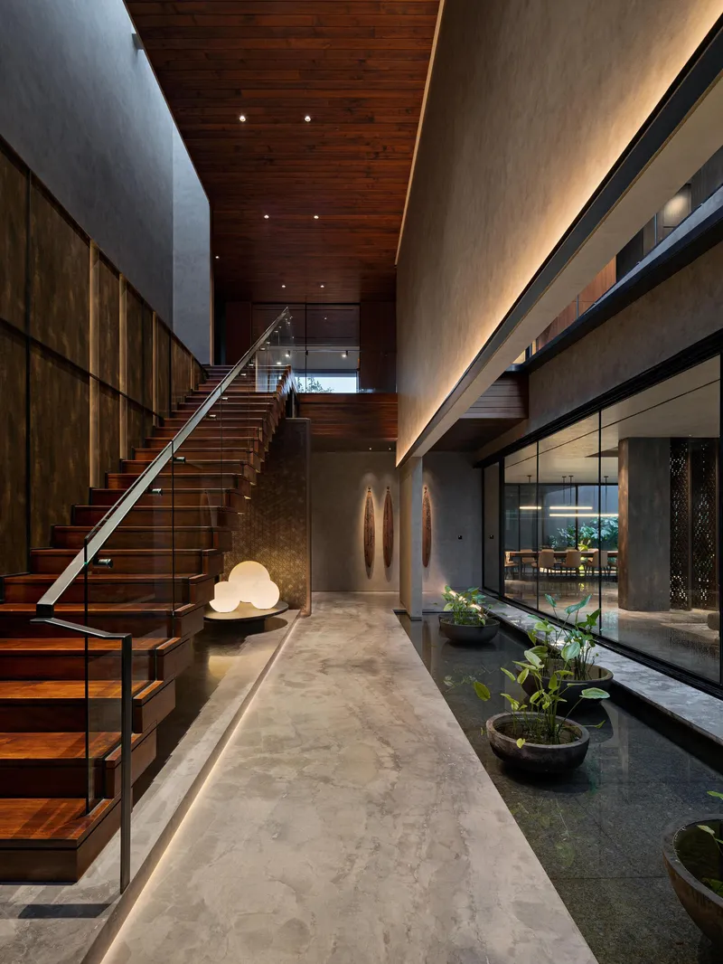 Entry hall with timber staircase and dark wood ceiling alongside glazed courtyard at dusk
