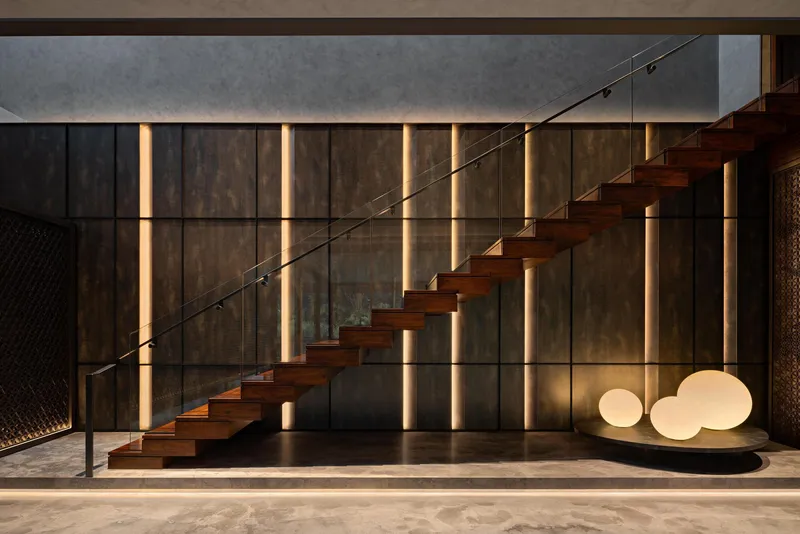 Cantilevered timber staircase with glass balustrade against vertical light strips at dusk