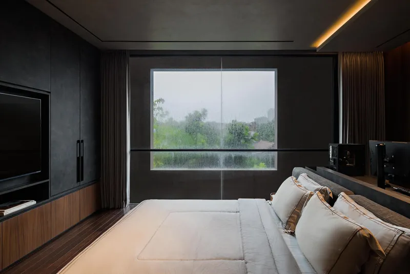 Bedroom with horizontal slot window framing greenery outside during rainfall