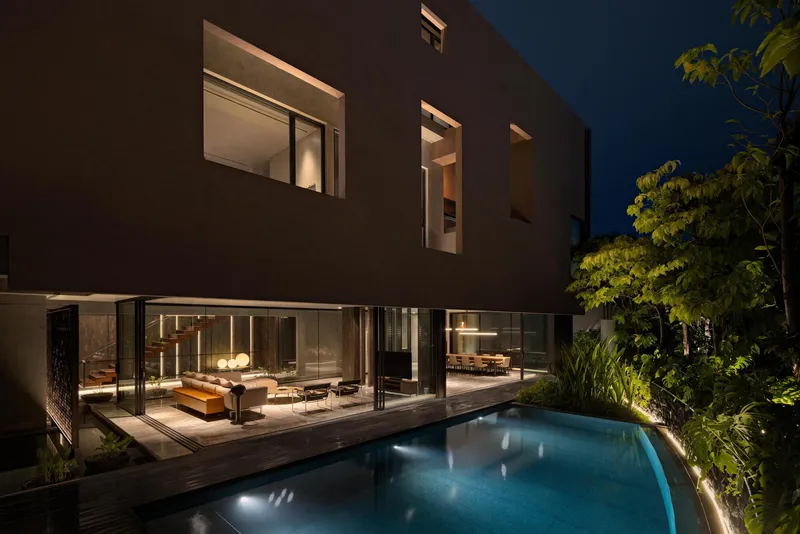 Rear facade at dusk with illuminated glass walls overlooking pool and timber deck