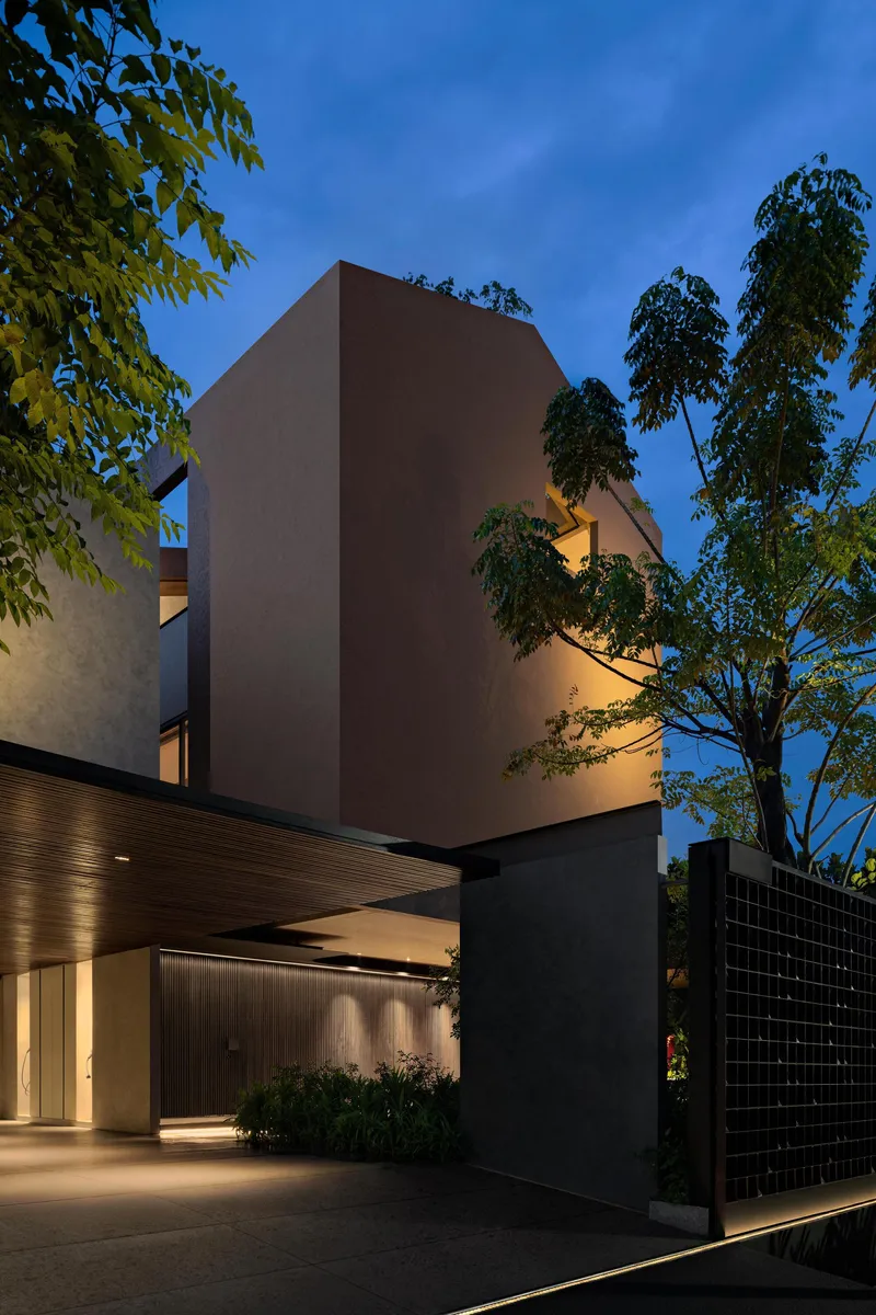 Entry facade at dusk with timber-lined canopy and tall trees framing stucco volumes