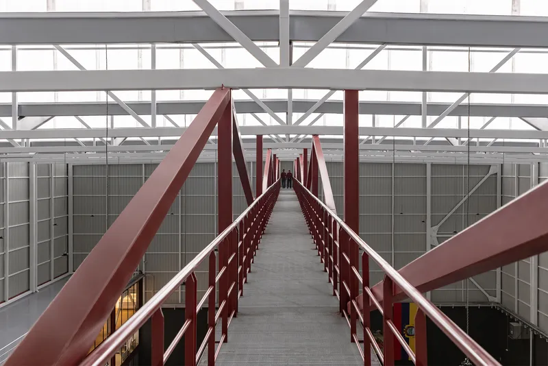 Enclosed steel bridge corridor with red railings and diagonal bracing viewed along its length