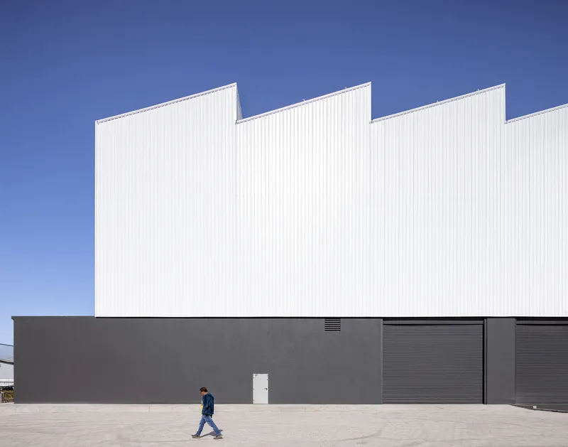 Street facade with dark grey base and white sawtooth roof form against a clear blue sky