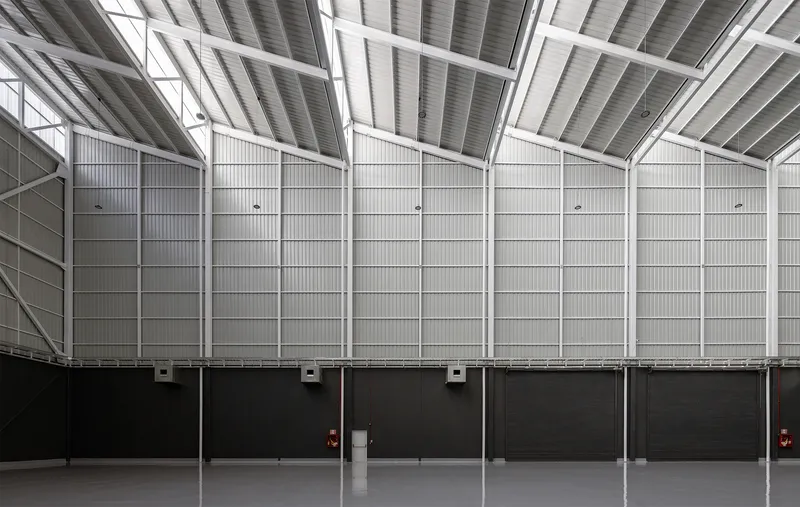 Interior wall of corrugated metal panels rising to meet angled skylights in the sawtooth roof above