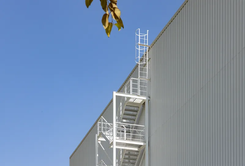 White painted steel egress stair against the corrugated metal cladding under clear blue sky