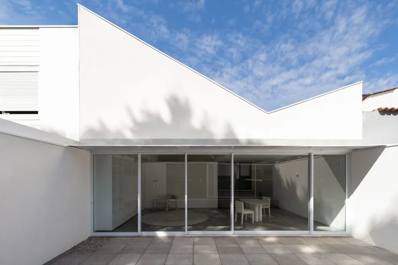 Interior courtyard with full-height glass doors and tree shadow cast across the white parapet walls