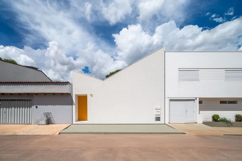 Street facade with white stucco walls and a recessed yellow entry portal under cumulus clouds