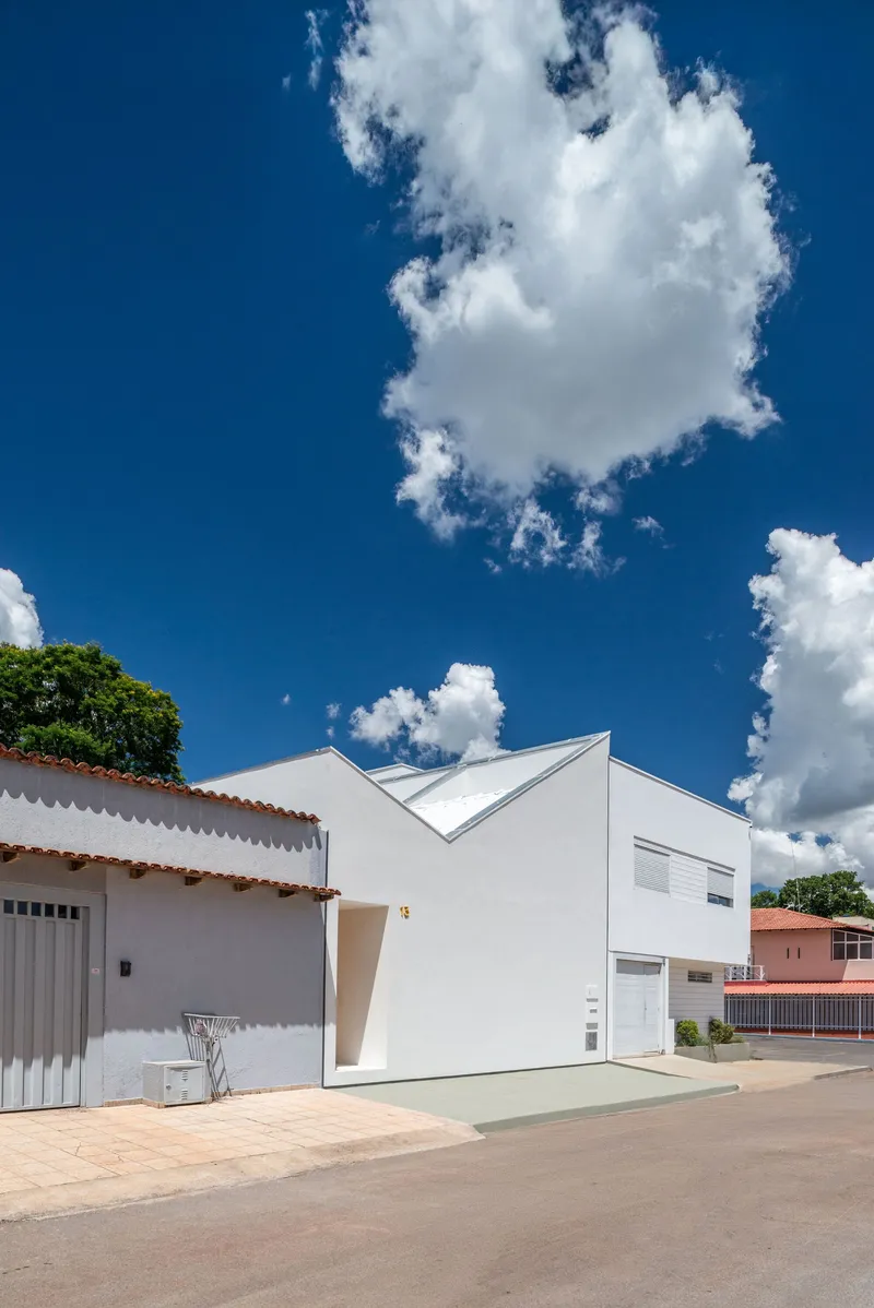 White plastered facade with angular roofline adjacent to a corrugated metal clad neighbor beneath blue sky