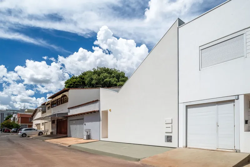 Street view of white volume with triangular roofline beside existing terracotta tiled structures and shopfronts