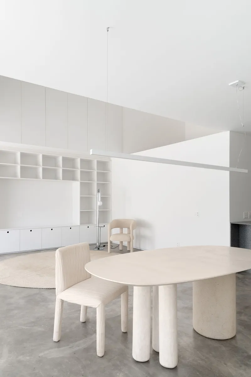 Dining area with pale wood table on cylindrical legs and built-in shelving beneath a sloped ceiling