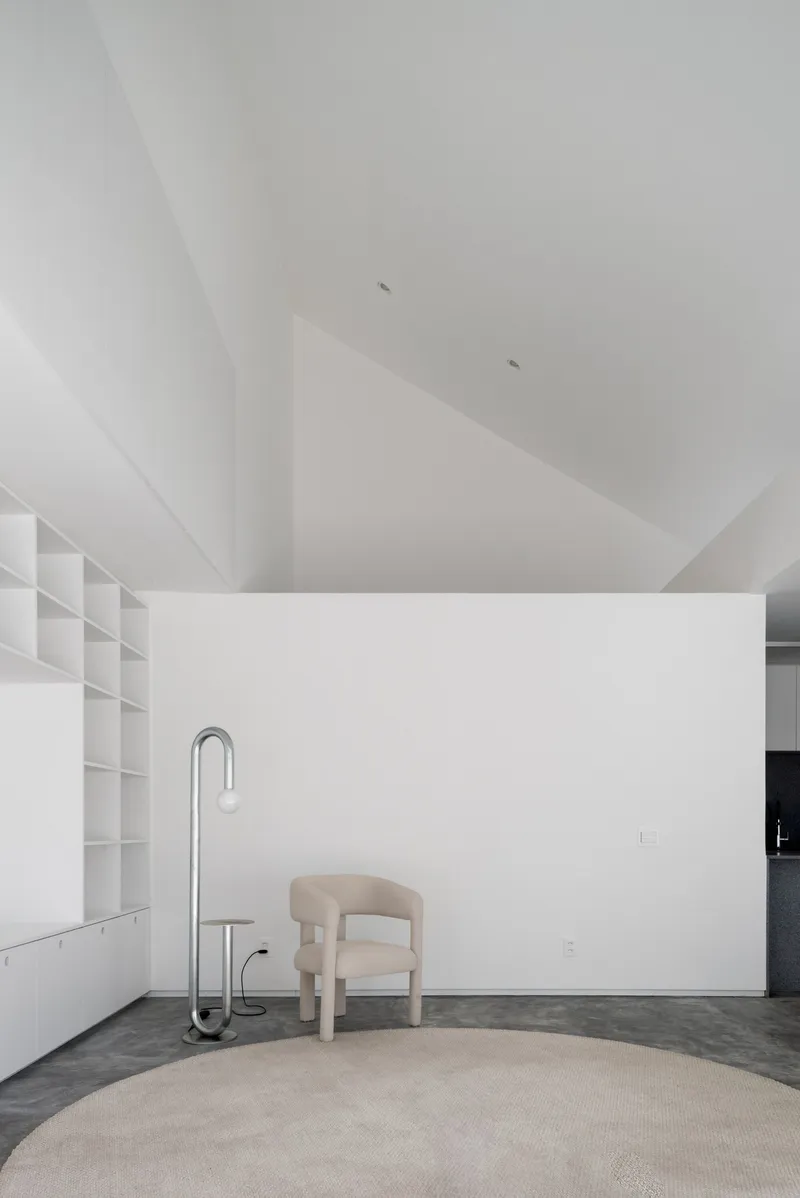 White interior room with faceted ceiling geometry and a beige upholstered chair on a round rug