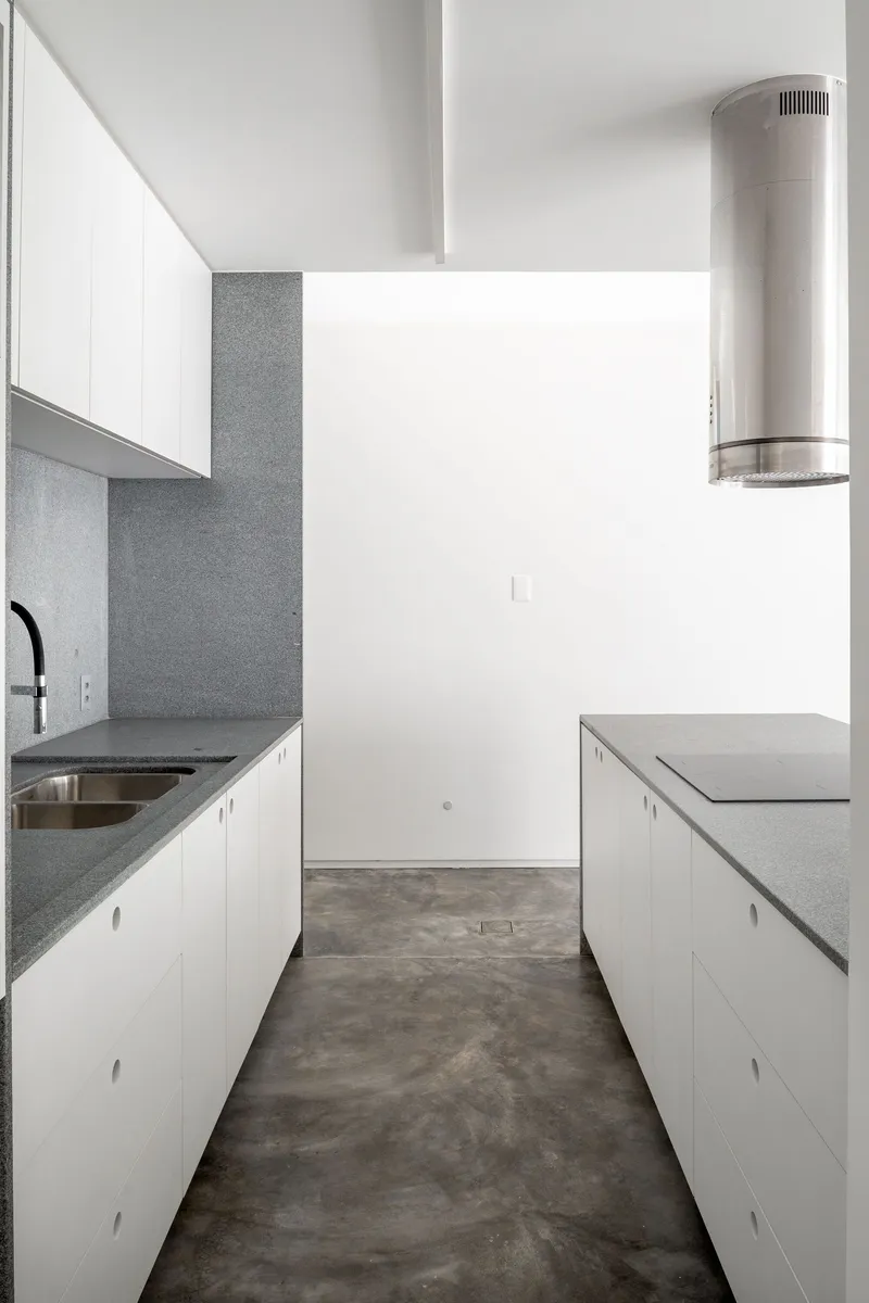 Galley kitchen with white cabinetry, grey terrazzo countertops and a cylindrical stainless steel range hood
