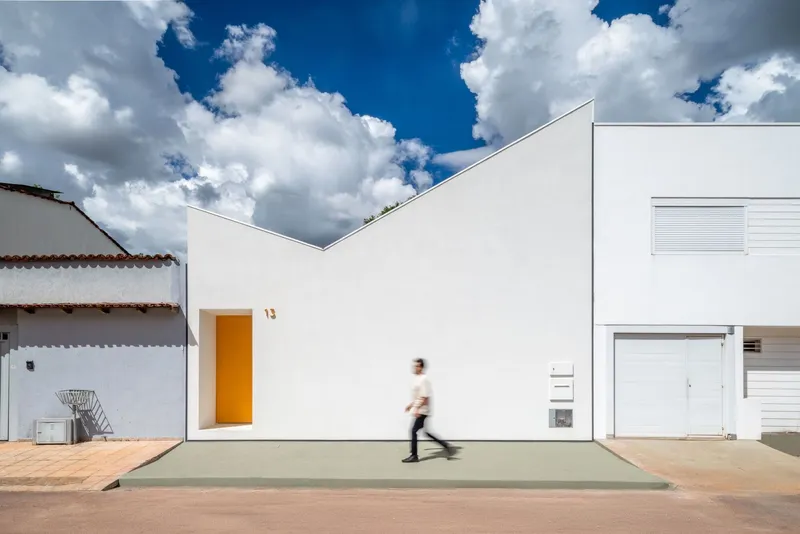 White stucco facade with recessed orange doorway and a person walking across the concrete entrance under blue sky