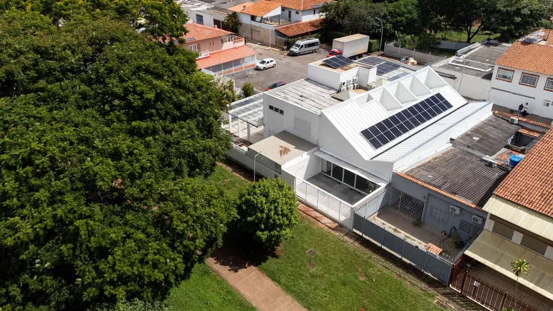 Aerial view of faceted white roof with solar panels nestled among terracotta-roofed neighbors and green trees