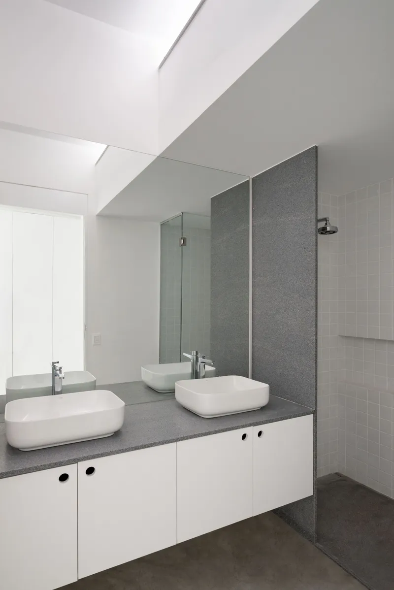 Bathroom vanity with two vessel sinks on grey terrazzo, white tile shower enclosure, and floating mirror
