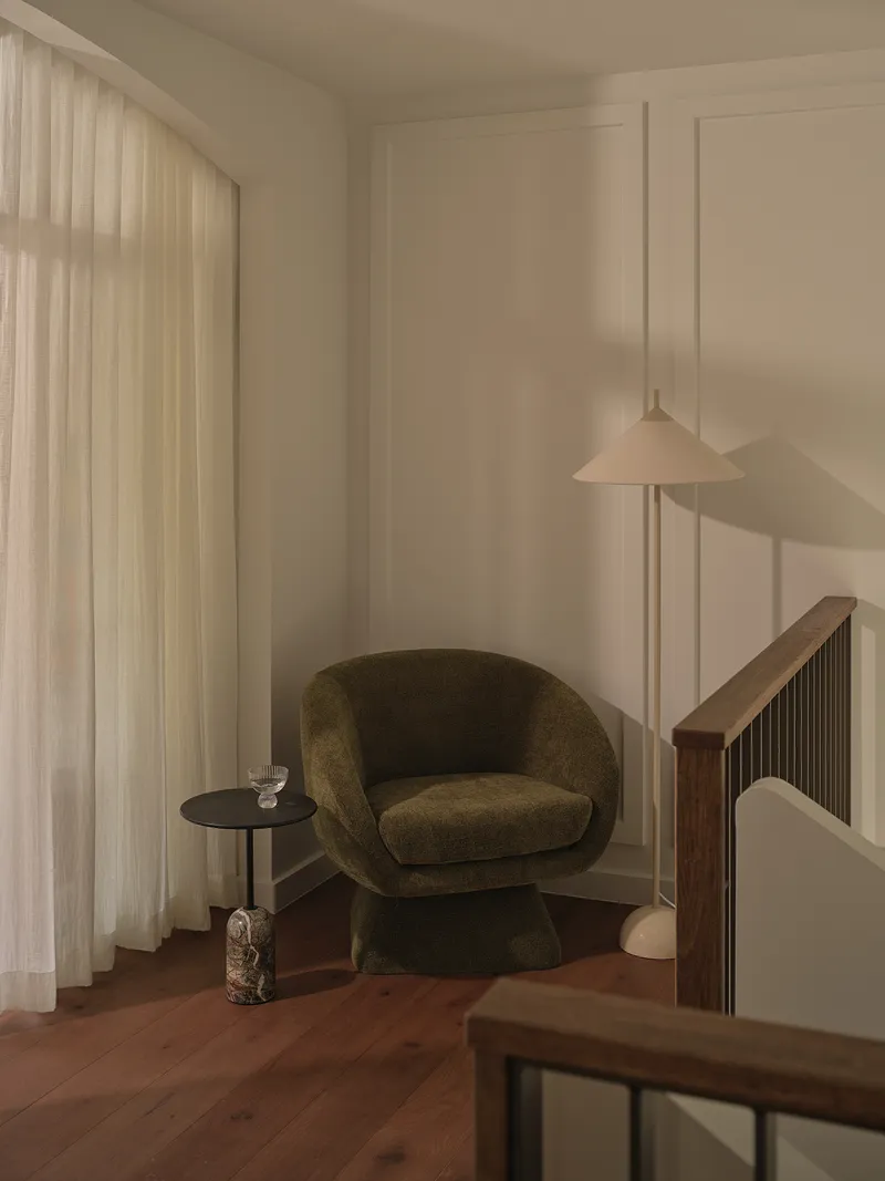 Reading corner with upholstered armchair, pendant light, and floor-to-ceiling curtains filtering afternoon light