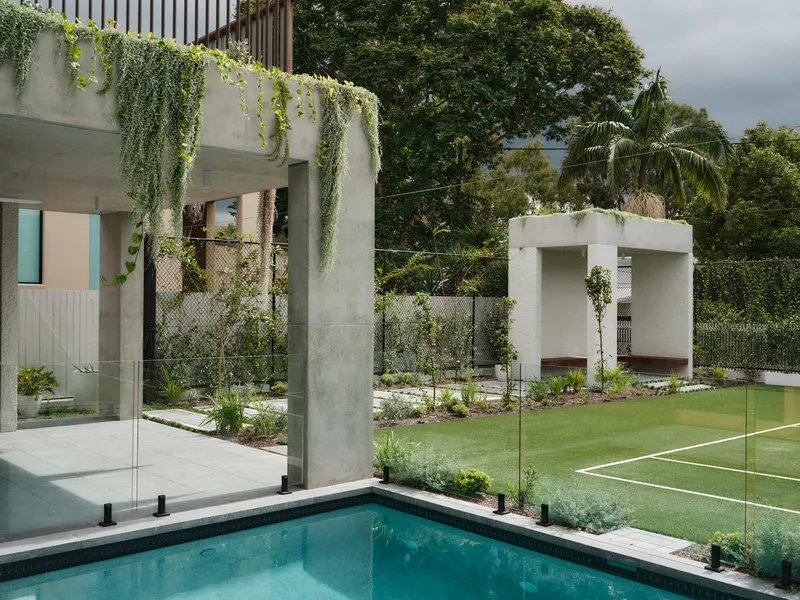 Rear garden view showing concrete pergola with trailing vines, glass balustrade pool edge and lawn under cloudy skies