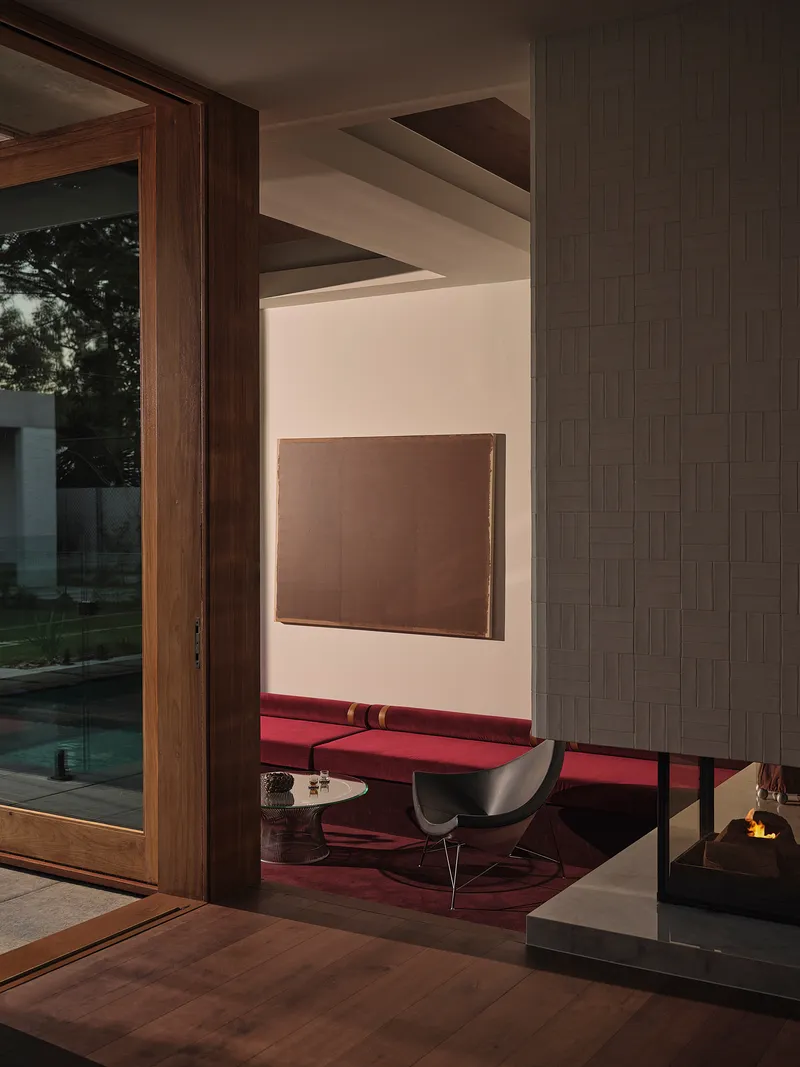 Interior corner showing timber door frame, woven tile wall panel and view through to seating in evening light
