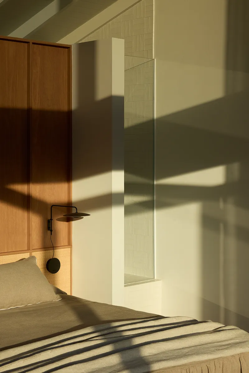 Bedroom with timber cabinetry and warm afternoon sunlight casting strong shadows across bed and walls