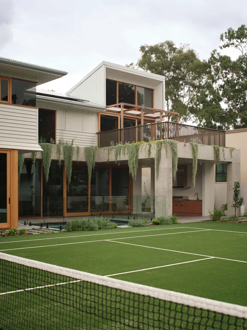 Garden facade with concrete planter wall, cascading greenery, timber balcony and tennis court under overcast sky