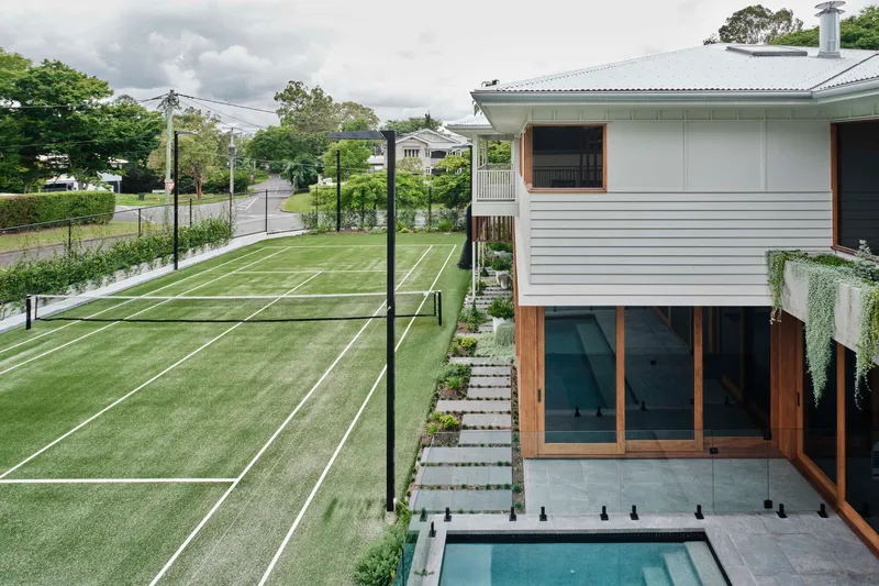 Elevated rear terrace with plunge pool and timber-framed glazing overlooking a grass tennis court