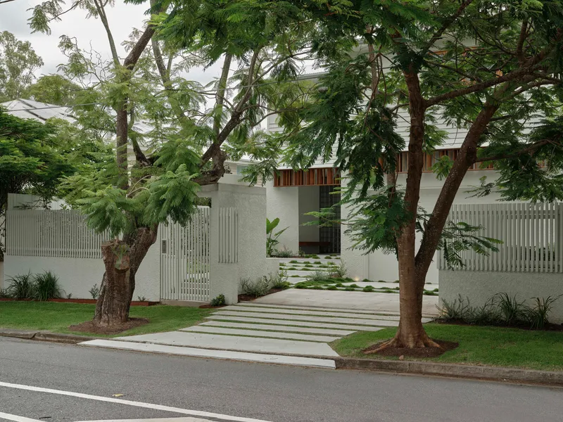 Street entrance framed by mature trees with vertical concrete slat screening and paved pathway