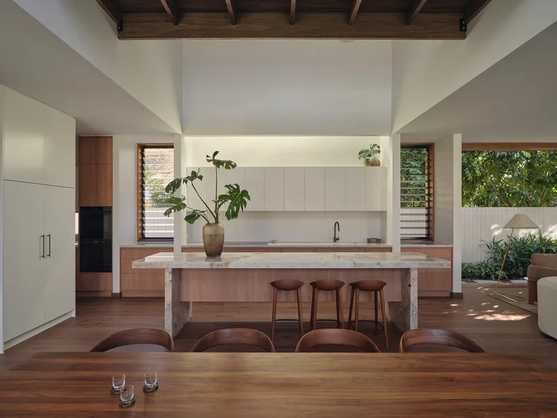 Open kitchen and dining area with timber island, exposed roof structure, and planted courtyard beyond