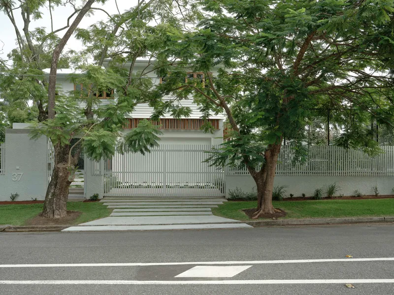 Street view of the white slatted fence and gate flanked by tall trees