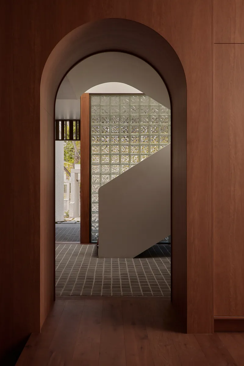 View through arched timber doorway to a curved staircase wall clad in translucent glass blocks
