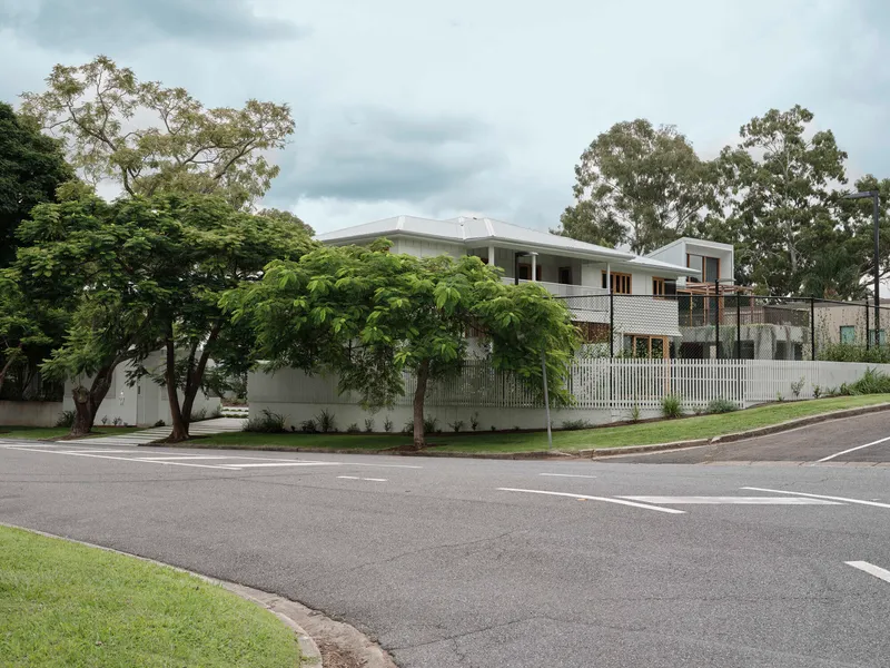 Street corner view showing white weatherboard cladding and corrugated metal roof beneath mature trees