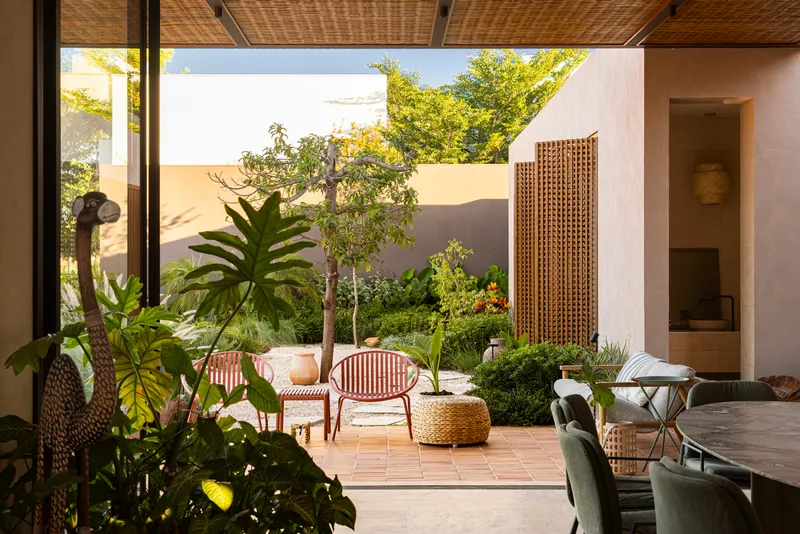 View from living space through woven ceiling to a planted courtyard with tile pavers and timber screens