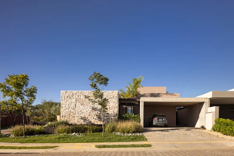 Street view of the textured stone wall and covered carport under a clear blue sky