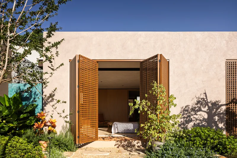 Perforated timber screens framing a bedroom entrance with tree shadows on the stucco wall