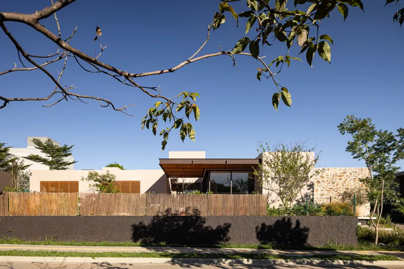 Street view of the stone and stucco facade with bamboo screening and tree branch shadows in afternoon light