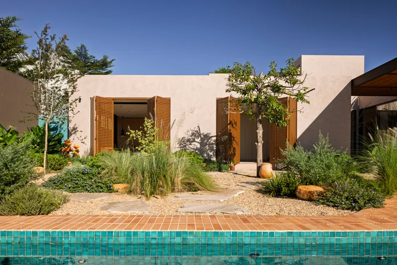 Poolside view of the courtyard facade with lattice shutters and native grasses in a gravel garden bed