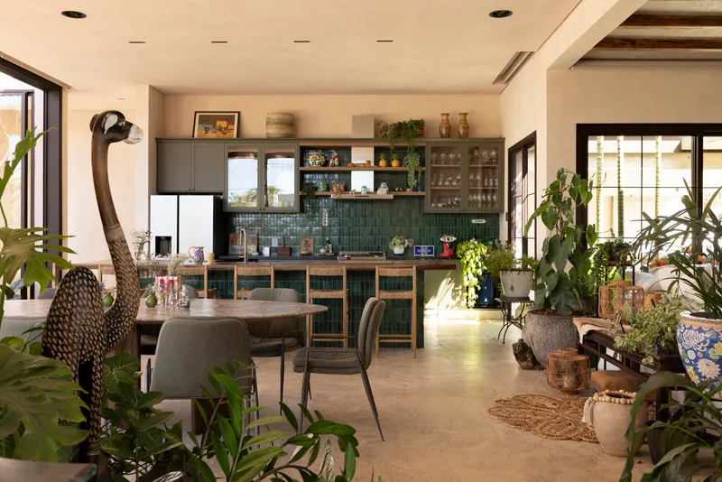 Open-plan kitchen and dining area with green tile backsplash, potted plants, and exposed timber ceiling beams