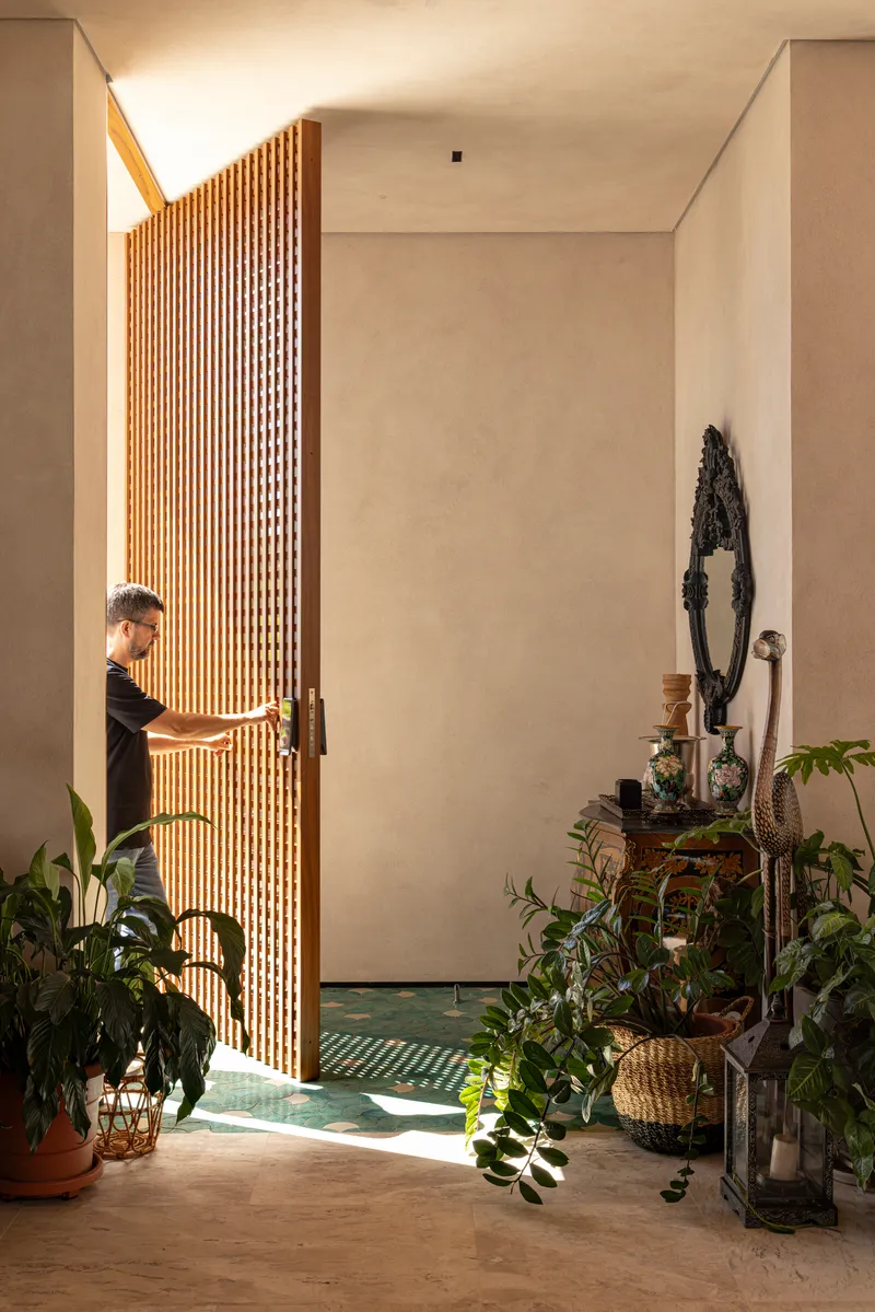 Entry foyer with curved vertical timber slat screen and person visible through the doorway beside potted plants