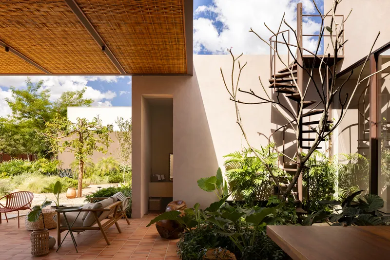 Covered patio with woven cane ceiling, spiral staircase, and planted courtyard under blue sky