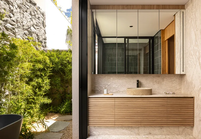 Bathroom vanity with stone countertop and timber cabinetry opening to bamboo courtyard