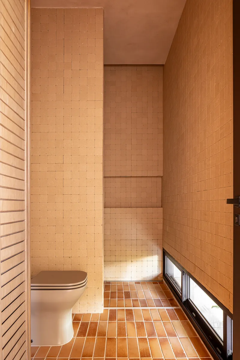 Tiled bathroom with timber wall panels and horizontal slit window at floor level