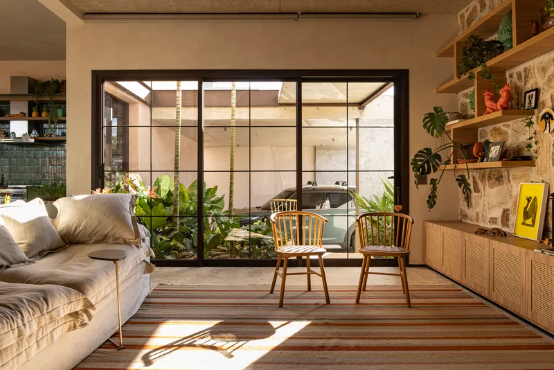 Steel-framed glazed wall separating the living area from a planted internal courtyard with spiral stair