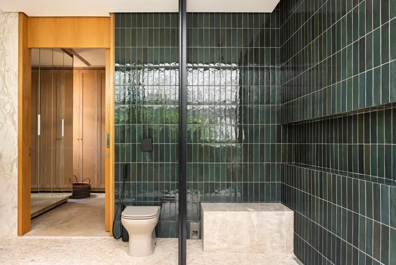 Bathroom with dark green vertical tile walls and a glass-enclosed shower overlooking a planted courtyard